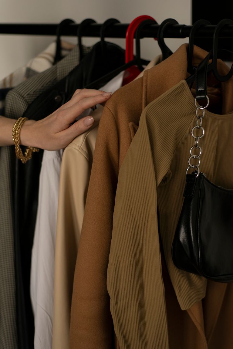 A hand picking clothes in a stylish wardrobe with neutral tones and a black handbag.