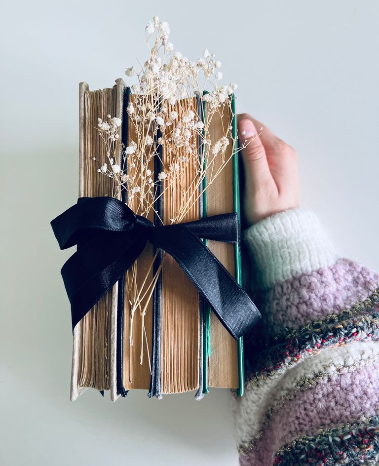 A stack of vintage books tied with a black ribbon and adorned with delicate flowers, held by a hand.