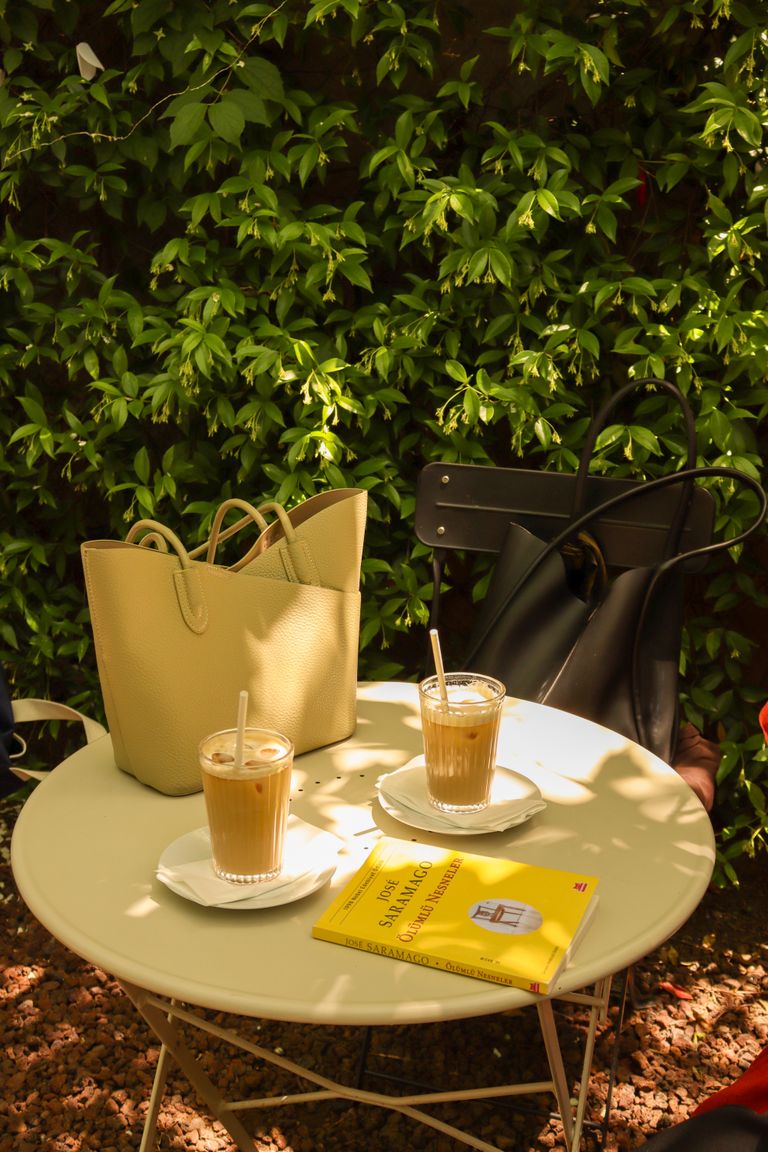 Sunny outdoor cafe table with iced coffee, bags, and a book, creating a relaxed ambiance.